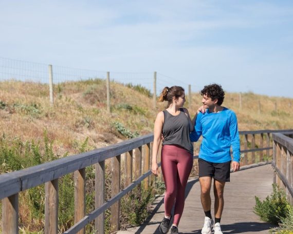 A couple in activewear strolling together on a sunny boardwalk in a natural setting.
